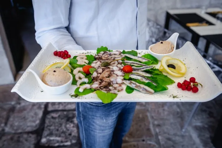  a man holding a plater of octopus carpaccio, fish pate and anchovies