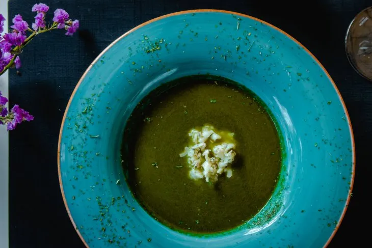  a teal plate with pumpkin soup and gorgonzola cheese with purple flowers on the side of the table