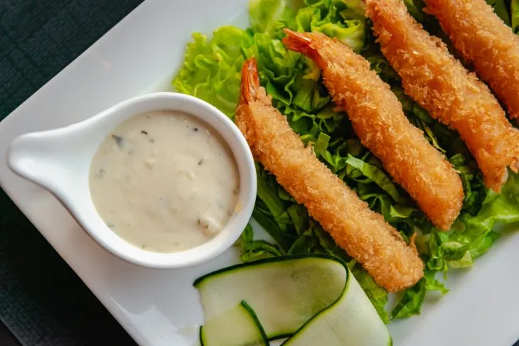  fried shrimp on a white plate on a bed of salad and tartar sauce on the side